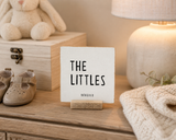 “The Littles,” a 4 x 4-inch shelf sitter in the black lettering on white distressed finish, styled on a sibling bookshelf.