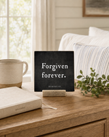 Forgiven Forever 4x4 Christian Shelf Sitter on a wood desk with a cream mug, greenery, a clothbound Bible, and a striped cushion.
