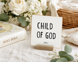“Child of God,” a 4 x 4-inch shelf sitter in the black lettering on white distressed finish, styled on a baptism celebration table.