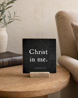 Christ in Me 4x4 Christian Shelf Sitter on a round wood side table beside an upholstered chair, neutral vase, and closed dark book.