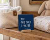 “For This Child I Prayed” 4 x 4-inch shelf sitter in the white lettering on dark blue finish, displayed on a changing table shelf.