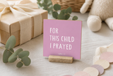 Close-up of “For This Child I Prayed,” a 4 x 4-inch shelf sitter in the white lettering on pink finish on a baby shower gift table.