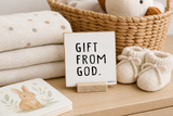 Gift from God,” a 4 x 4-inch shelf sitter in the black text on white distressed finish, styled in a new baby gift basket.
