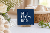 “Gift from God” 4 x 4-inch shelf sitter in the white text on dark blue finish, displayed on a baby dedication table.