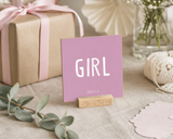 Close-up of “Girl,” a 4 x 4-inch shelf sitter in the white lettering on pink finish on a baby shower gift table.