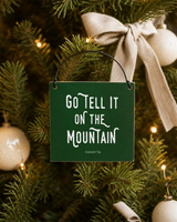 Dark Green 4x4 Go Tell It on the Mountain ornament with metal wire hanger on a warm fir with soft linen bows, ivory balls, and tiny amber lights.