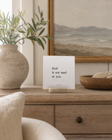 God Is Not Mad at You 4x4 Christian shelf sitter with natural wood base, styled in a coastal living room console scene.