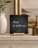 God Is With Us 4x4 Christian Shelf Sitter on a plaster mantel with coastal artwork, a neutral vase, and an antique brass vessel.