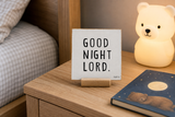 “Good Night Lord,” a 4 x 4-inch shelf sitter in the black text on white distressed finish, styled on a bedside nightstand.