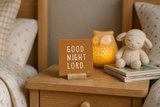 Close-up of “Good Night Lord,” a 4 x 4-inch shelf sitter in the white text on burnt orange finish on a shared room nightstand.