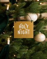 Gold 4x4 Holy Night ornament with metal wire hanger on a refined tree with clip-on candle lights, cream baubles, and deep green ribbon.