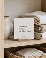 I Don't Like Humans, but I Love Them 4x4 Christian shelf sitter with natural wood base, styled in a linen cabinet shelf scene.