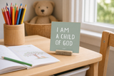 Close-up of “I Am a Child of God,” a 4 x 4-inch shelf sitter in the white lettering on light green finish on a homeschool desk.