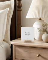Let God Love You 4x4 Christian shelf sitter with natural wood base, styled in a limestone living room mantel scene.