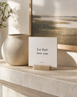 Let God Love You 4x4 Christian shelf sitter with natural wood base, styled in a coastal bedside table scene.