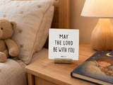 “May the Lord Be with You,” a 4 x 4-inch shelf sitter in the black lettering on white distressed finish, styled on a bedside nightstand.