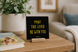 Close-up of “May the Lord Be with You,” a 4 x 4-inch shelf sitter in the gold lettering on black finish in a family prayer corner.