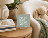 Close-up of “May We Never Lose Our Wonder,” a 4 x 4-inch shelf sitter in the white lettering on green distressed finish in a reading nook.