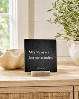 May We Never Lose Our Wonder 4x4 Christian Shelf Sitter on a light console by a window with a sculptural stone bowl and leafy branch.