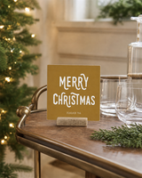 Gold 4x4 Merry Christmas Christmas Shelf Sitter in a dining room bar cart with its rustic wood slot stand.