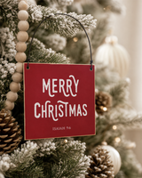 Red 4x4 Merry Christmas ornament with metal wire hanger on a softly flocked tree with natural wooden beads, cream ornaments, and pinecones.