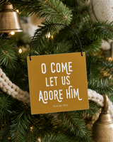 Gold 4x4 O Come Let Us Adore Him ornament with metal wire hanger on a Coastal Pottery Barn tree with woven cream garland and aged brass accents.