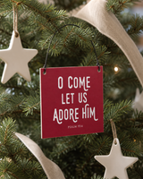Red 4x4 O Come Let Us Adore Him ornament with metal wire hanger on a neutral tree with matte white ceramic stars and linen ribbon.
