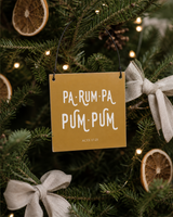 Gold 4x4 Pa-Rum-Pa-Pum-Pum ornament with metal wire hanger on a natural fir with dried citrus, linen bows, and tiny white lights.