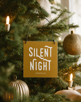 Gold 4x4 Silent Night ornament with metal wire hanger on a tree with candle lights, antique gold ornaments, and cream ribbon.
