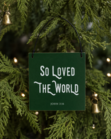 Dark Green 4x4 So Loved the World ornament with metal wire hanger on a dense green tree with petite brass bells and restrained white lights.