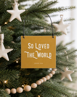 Gold 4x4 So Loved the World ornament with metal wire hanger on an organic-modern tree with ivory ceramic stars and natural bead garland.