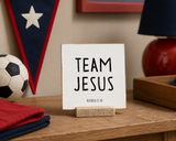 “Team Jesus,” a 4 x 4-inch shelf sitter in the black lettering on white distressed finish, styled on a sports bedroom desk.