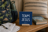 Team Jesus,” a 4 x 4-inch shelf sitter in the white lettering on dark blue finish, styled in a kids camp packing bench.