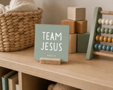 Close-up of “Team Jesus,” a 4 x 4-inch shelf sitter in the white lettering on green finish on a playroom cubby.