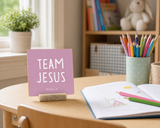 “Team Jesus” 4 x 4-inch shelf sitter in the white lettering on pink finish, displayed on a homeschool desk.