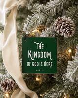 Dark Green 4x4 The Kingdom of God Is Here ornament with metal wire hanger on a lightly flocked tree with frosted pinecones and ivory velvet ribbon.