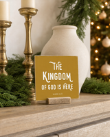 Gold 4x4 The Kingdom of God Is Here Christmas Shelf Sitter in a christmas living room console with its rustic wood slot stand.