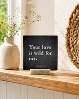 Your Love Is Wild for Me 4x4 Christian Shelf Sitter on a light shelf with wildflowers, a stone vase, and woven wall texture.
