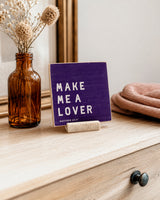 Make Me a Lover 4x4 Christian Shelf Sitter on a light wood dresser with an amber bottle, dried flowers, and folded textiles.