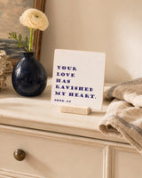 Your Love Has Ravished My Heart 4x4 Christian Shelf Sitter on a cream dresser with a navy vase, flower, and neutral textiles.